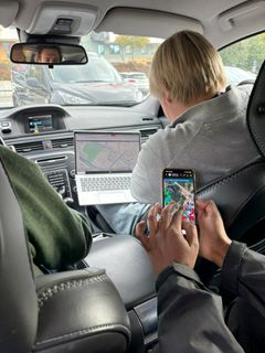 En person bruker en bærbar PC med kart på skjermen i baksetet av en bil, mens en annen holder en mobil med et kart på skjermen. Sjåføren ser på veien.
