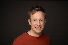 Person med kort hår og rød genser smiler mot kameraet.