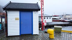 Ei hvit målehytte med blå dør ved kaien i Bergen.