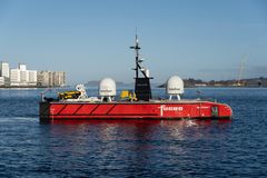 En stor rød USV ved navn Blue Eclipse® fra Fugro, ligger til sjøs med bylandskap i bakgrunnen.