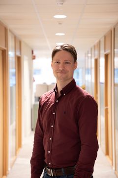 En mann i burgunderrød skjorte står i en kontorkorridor.