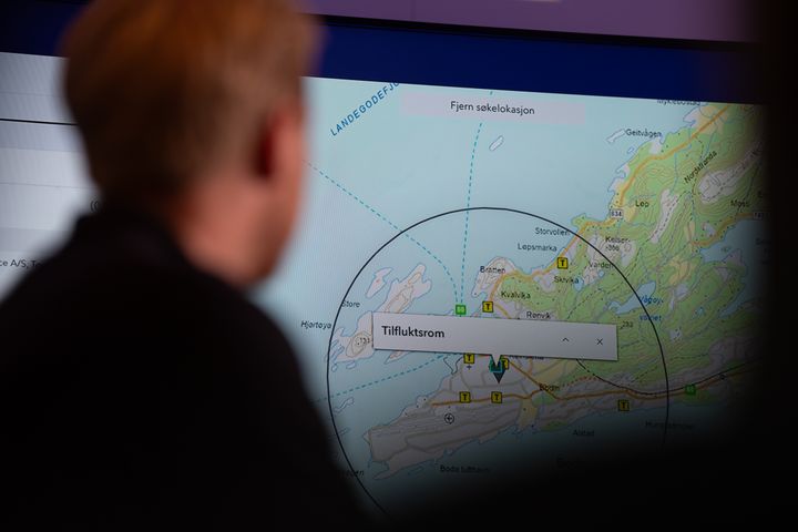 En person ser på et kart over en kystregion med markeringer og tekstboksen "Tilfluktsrom".