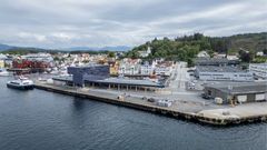 Utsikt over Florø havn med flere båter ved kaia, bygninger og grønne åser i bakgrunnen.