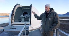 Ole Johan Ekeli Klingan står ved siden av satellittavstandsmåleren med laser (SLR) på jordobservatoriet i Ny-Ålesund.