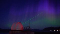 SLR-instrument ved Ny-Ålesund sender grønn laserstråle mot nordlyshimmelen.