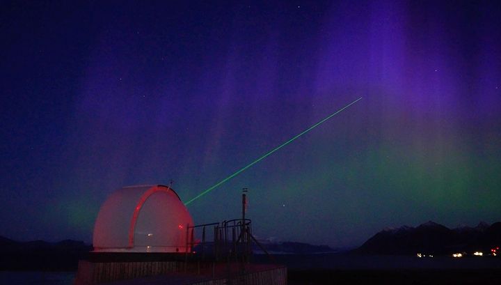 SLR-instrument ved Ny-Ålesund sender grønn laserstråle mot nordlyshimmelen.