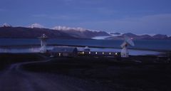 Norges geodetiske jordobservatorium i Ny-Ålesund i kveldslys, foran fjell og fjord.