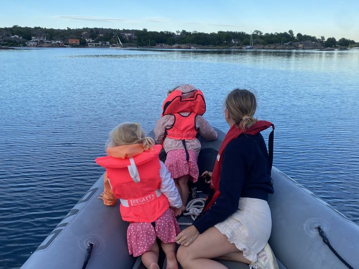 Tre kvinnelige personer i front av en båt. De ser foran seg, og har ryggen mot kameraet. To av personene er barn, den andre en dame i tredveårene. Alle tre har på redningsvest.