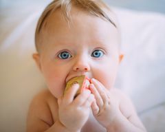 Liten baby med veldig blå øyne har en trekloss i munnen. Foto.