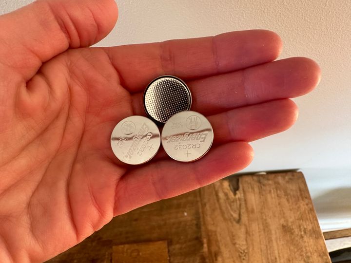 En utstrakt hånd der det ligger tre knappcellebatterier i håndflaten.