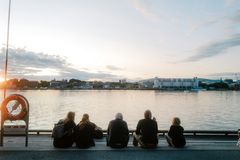 5 personer sitter ved siden av hverandre på en brygge og ser utover sjøen. Man ser en livbøye til venstre i bildet. Foto.