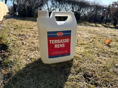 En hvit flaske med Terrasserens skrevet på etiketten står alene på en gressplen. Foto.