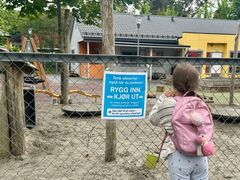 Jente som lener seg mot et gjerde foran en barnehage. Det henger et skilt på gjerde der det står: Rygg inn - kjør ut.
