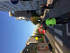 En sykkelsti langs en travel bygate med syklist i grønn jakke. Det er biler og en lastebil i trafikken, med moderne bygninger på begge sider.