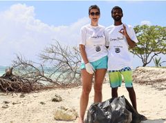 Mann og kvinne på strand med plastsekk foran seg.