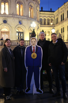 En gruppe mennesker poserer med en pappfigur foran Stortinget.