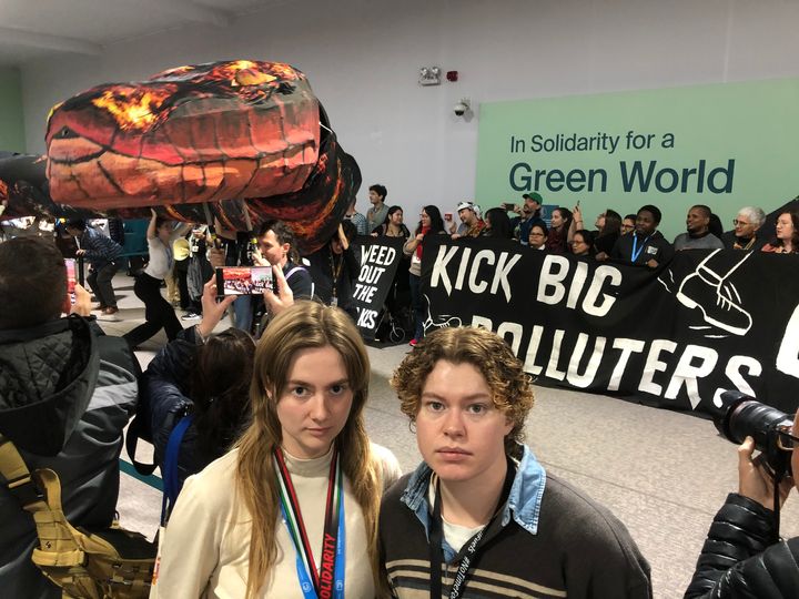 Spires delegater står foran demonstranter som holder et banner med teksten "Kick Big Polluters Out" foran en vegg med teksten "In Solidarity for a Green World".