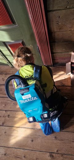 En konservator med gul vest sitter på knærne inntil en dør i Finnegården. Hun har på en gul vest og en støvsuger på ryggen.