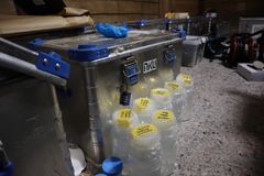 En stålkoffert med konserveringsutstyr. Foran kofferten står det flere gjennomsiktige glass med gul tape på lokket. Det står det beskrevet hva som er inni glassene.