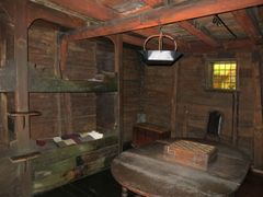 Et innredet rom slik det så ut i et Hansahus på 1700-tallet. Til venstre i rommet er fire veggfaste senger malt i grønt. Midt i rommet er et ovalt bord i tre med et sjakkbret oppå, og i hjørnet står en stol. Veggene er av laftet tømmer, og takbjelkene er malt røde.