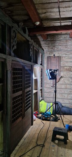 En konservator ligger på gulvet halvveis under et skap, for å kunne støvsuge flatene ingen kan se. Rommet er mørkt og hun jobber i lys av en arbeidslampe.