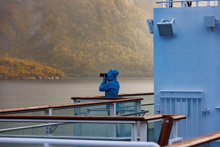 En gjest om bord på Havila Kystruten fotograferer fra dekk langs norskekysten.