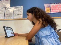 Jente på barneskolen med langt mørkt hår og blå topp leser en artikkel om krig på Lille norske leksikon på en ipad
