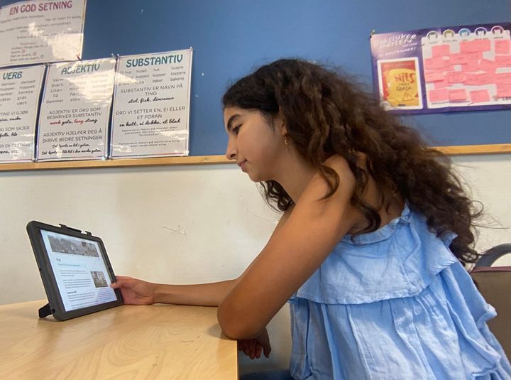 Jente på barneskolen med langt mørkt hår og blå topp leser en artikkel om krig på Lille norske leksikon på en ipad