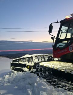 Snøprepareringsmaskin arbeider i solnedgangen ved en snødekket bakke.