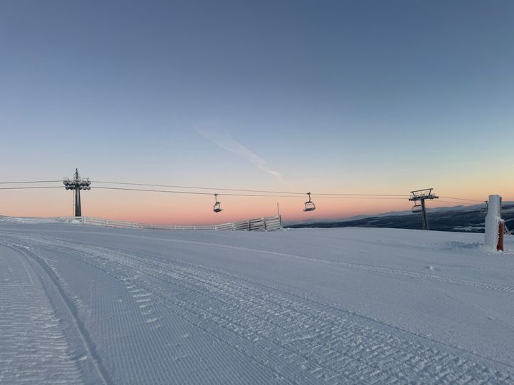 Skitrekk på et snødekt fjell i soloppgang, med pastellfarget himmel i bakgrunnen.