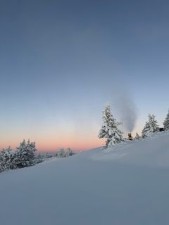 Snødekket landskap med snøkanoner i drift under en klar, fargerik himmel.