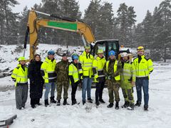 Mennesker i refleksvest i rekke foran gravemaskin i vintervær.