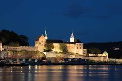 Akershus festning i Oslo, nattbilde med opplyste murer og tårn, reflektert i vannet.