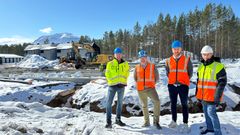 Fire menn i verneutstyr står foran en byggeplass i snødekt landskap.