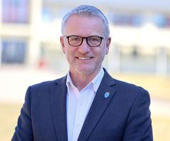 En mann i dress og briller smiler mot kameraet.