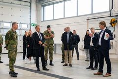 En gruppe mennesker, inkludert personer i militæruniform, står inne i en stor bygning under en befaring.
