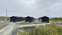 Bygninger med mørk fasade i Camp Akkasæter omgitt av grå veier og vegetasjon. En kran står i bakgrunnen.