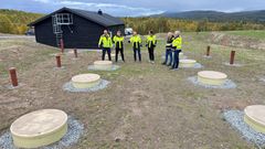 Fem personer i gule jakker inspiserer et utendørs anlegg med rund betongdekker.