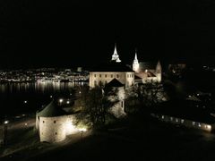 Nattbilde av Akershus slott, opplyst mot en mørk bakgrunn.