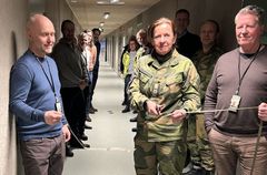 Oberst May Brith Valen-Odlo klipper snoren ved åpningen av en ny militærforlegning i Rusta leir, Bardufoss. Gruppe mennesker står langs veggene i en korridor.