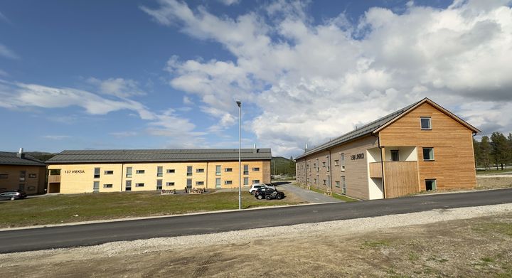 To bygninger med moderne design ved en vei under en blå himmel.