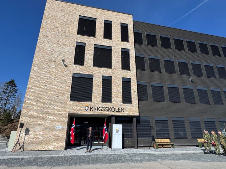 4-etasjes bygg i tegl og tre. Mann taler foran inngangsdør.