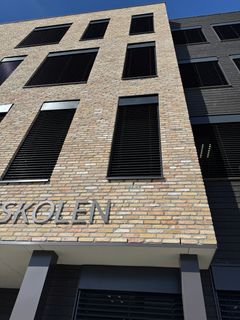 Nærbilde av murfasade med vinduer med svarte persienner.