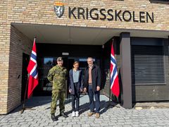 Tre personer på rekke foran nytt bygg med norske flagg på hver side.