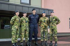 Fem personer i militæruniformer står sammen og smiler foran en bygning.