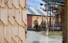 Vegg med trepanel i front, med trebygg og furu i bakgrunnen.