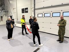 Flere mennesker står i en hall og hører på en mann i militær bekledning snakke.