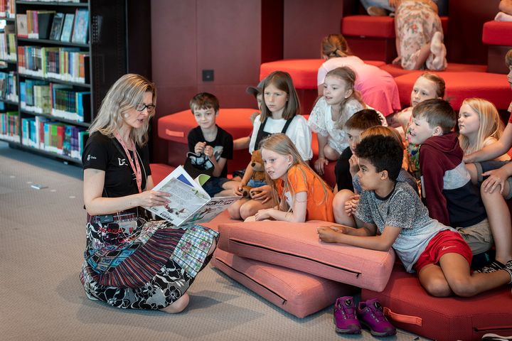 En voksen person leser høyt fra en bok til en gruppe barn på Deichman Bjørvikas barneavdeling.