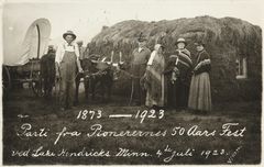 En gruppe mennesker står foran en stor stabel med høy og to okser. Teksten på bildet sier "Parti fra Pionerernes 50 Aars Fest ved Lake Hendricks Minn. 4. Juli 1923."