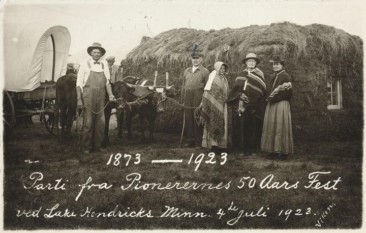 En gruppe mennesker står foran en stor stabel med høy og to okser. Teksten på bildet sier "Parti fra Pionerernes 50 Aars Fest ved Lake Hendricks Minn. 4. Juli 1923."